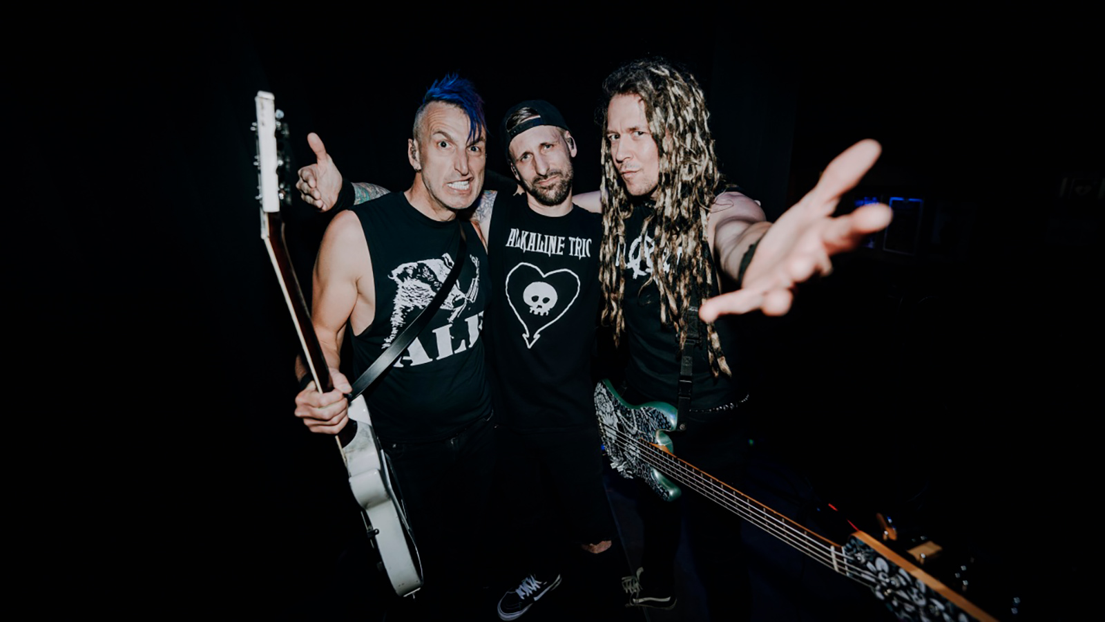 Three members of WIZO posing backstage with guitars against a dark background